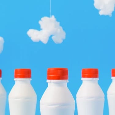 Milk bottles with red cap and light blue background
                    with clouds